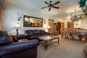 A living room with a brown leather sofa, a coffee table, a ceiling fan, a dining area with wooden chairs and a table, and a large mirror on the wall. - CL3105 | Comfortable Mountain Living | A/C | Close to Slopes (Steamboat Springs)