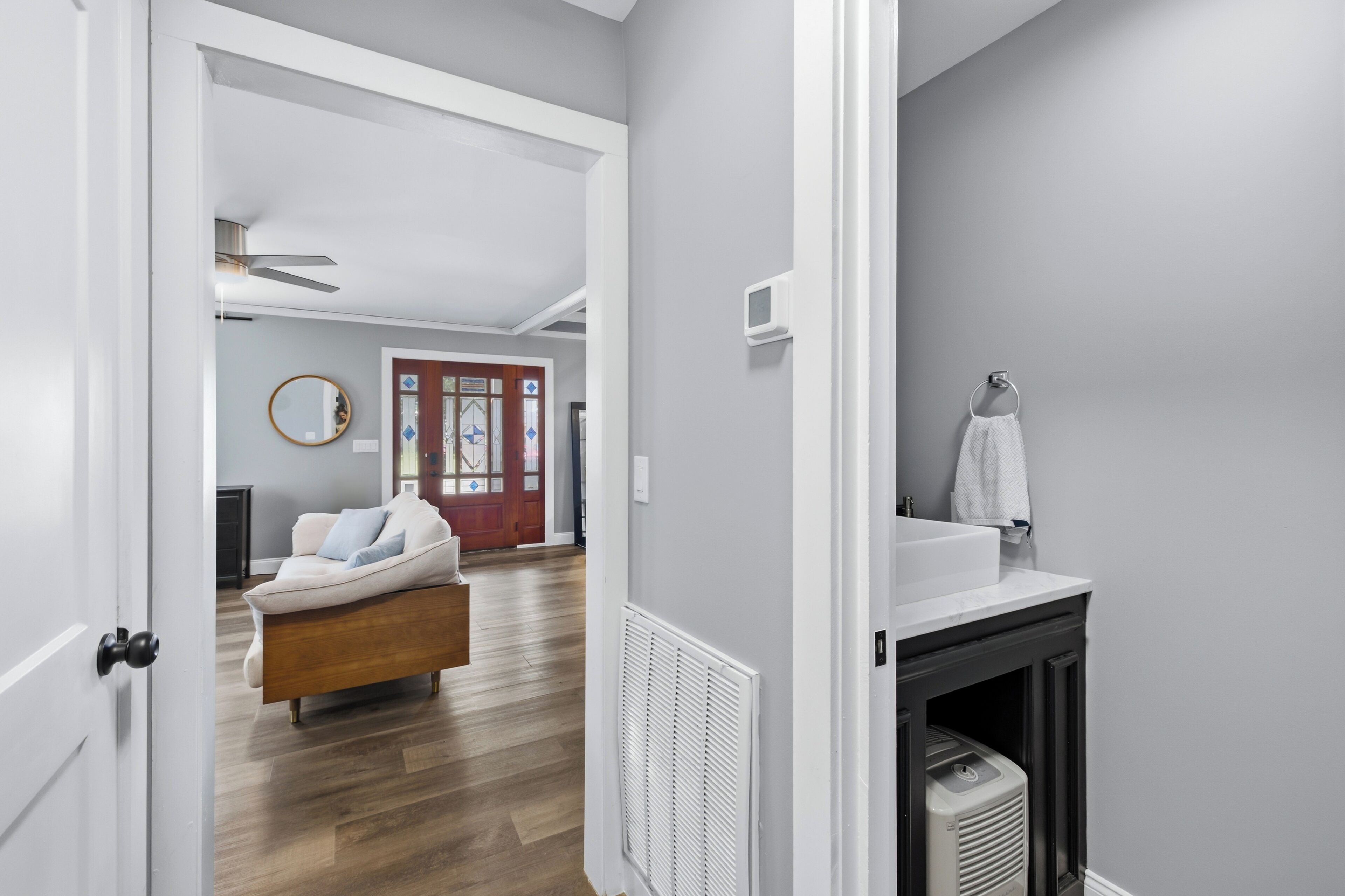 Un intérieur moderne avec un plancher en bois, un canapé blanc, une cheminée et une salle de bain équipée d’un porte-serviettes.