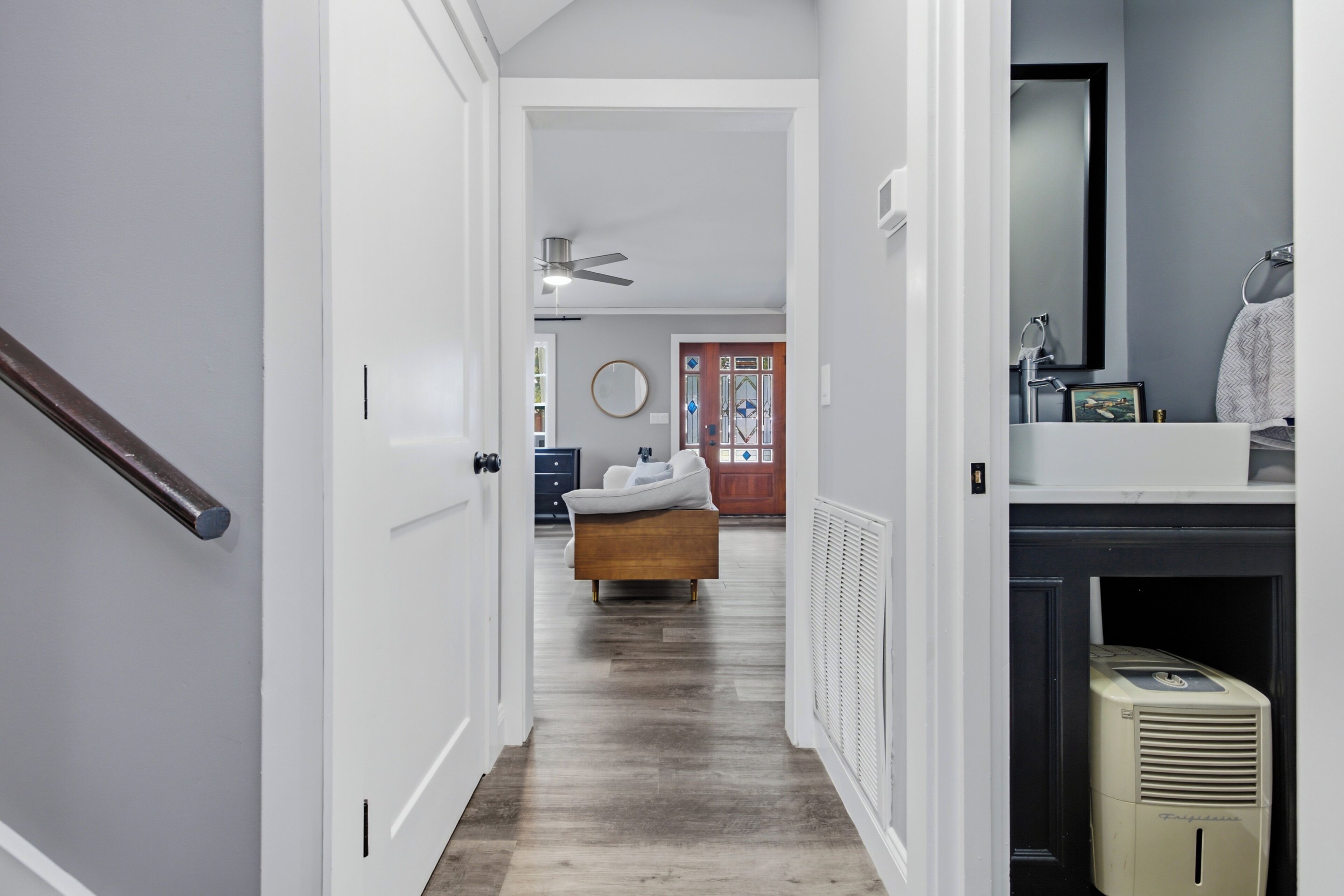 A hallway with a bed, a radiator, a mirror, and a door leading to another room.