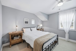 A bedroom with a bed, nightstands, a ceiling fan, and a window with curtains.