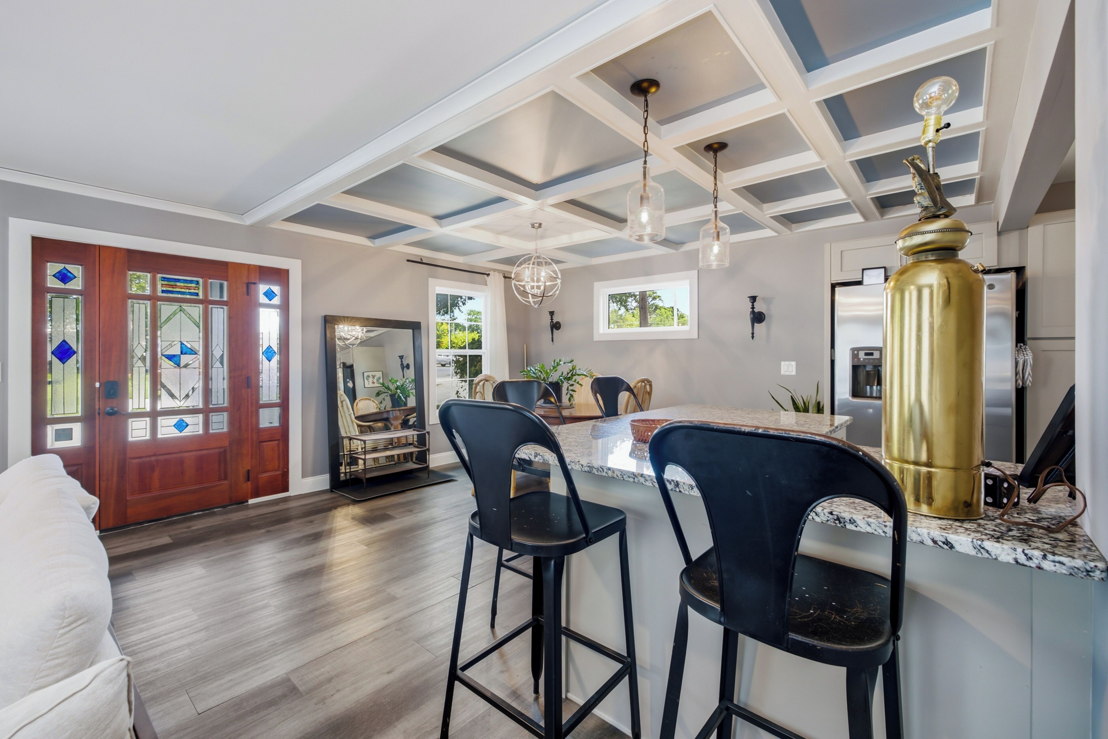 A modern kitchen with a central island, bar stools, a refrigerator, and a pendant light.
