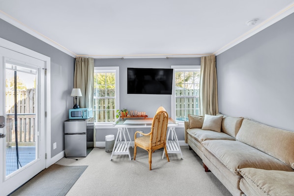 A modern living room with a sofa, a dining table, and a TV mounted on the wall.