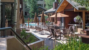 Ein Außenbereich mit Terrasse, Tischen, Stühlen, Sonnenschirmen und einem Pool.