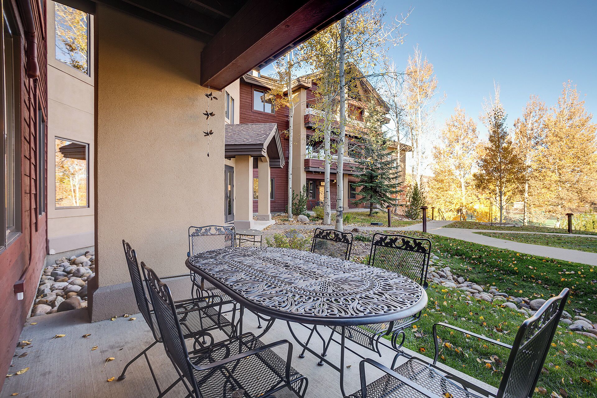 An outdoor patio with a round metal table and chairs, a stone pathway, and a building with a wooden facade in the background.