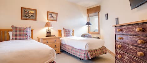 Un dormitorio con dos camas, un aparador de madera, un ventilador de techo y cuadros en la pared.