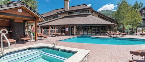 A pool area with lounge chairs, a hot tub, and a building with large windows.
