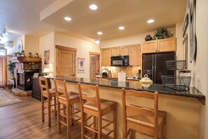 A kitchen with wooden cabinets, a black refrigerator, a microwave, and a bar area with wooden chairs. - CL3204 | Updated Condo with Beautiful Décor | A/C | Close to Mtn (Steamboat Springs)