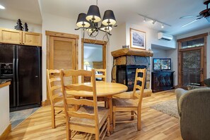 A dining area with wooden chairs and a table, a black refrigerator, a stone fireplace, and a television on a wooden stand. - CL3205 | Great Family Condo | A/C | 10 Hot Tubs | Close to Slopes (Steamboat Springs)