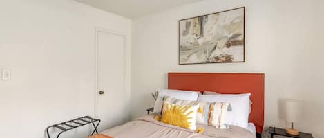 Un dormitorio con cama, ventilador de techo, una puerta y un cuadro abstracto colgado en la pared.