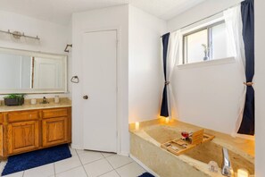 Un bagno con un mobile bagno in legno, uno specchio grande, una finestra con tende e un tappeto blu.
