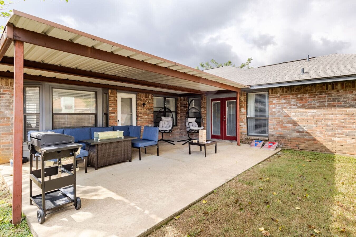 A covered patio area with outdoor seating, a grill, and a swing chair.