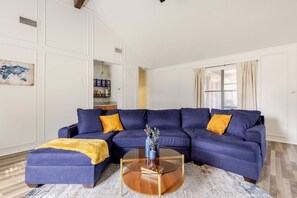 Ein Wohnzimmer mit einem Ecksofa, einem Couchtisch und einer Küchenzeile im Hintergrund.