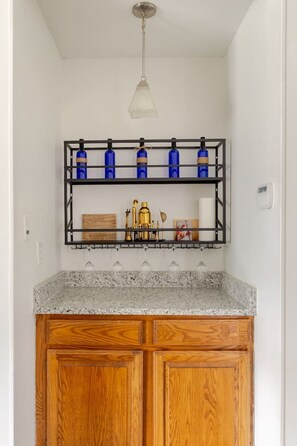 Eine Küche mit Granit-Arbeitsplatten, Holzschränken, einer Pendelleuchte und einem Regal mit blauen Flaschen und Küchenutensilien.