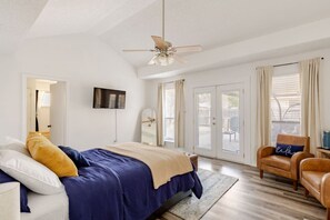 Una camera da letto con un letto, un ventilatore a soffitto, una TV e vista sull'esterno tramite una porta scorrevole in vetro.