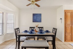 Ein Esszimmer mit Esstisch für vier Personen, einem Deckenventilator und einem blauen abstrakten Gemälde an der Wand.