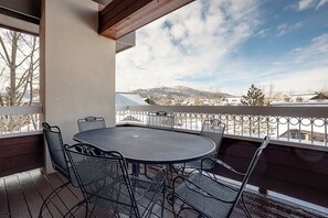 Ein Balkon mit einem runden Metalltisch und Stühlen, der Blick auf eine verschneite Landschaft und Gebäude gewährt.