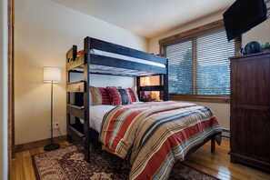 Ein Stockbett mit gestreifter Bettdecke, eine Stehlampe und ein Fenster mit Jalousien.