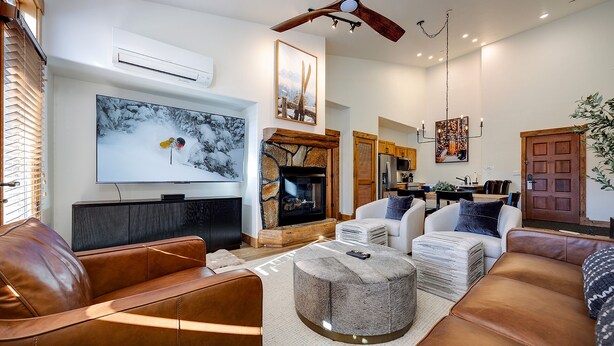 Una sala de estar moderna con sofás de cuero, una chimenea de piedra, un televisor de pantalla plana y un ventilador de techo.