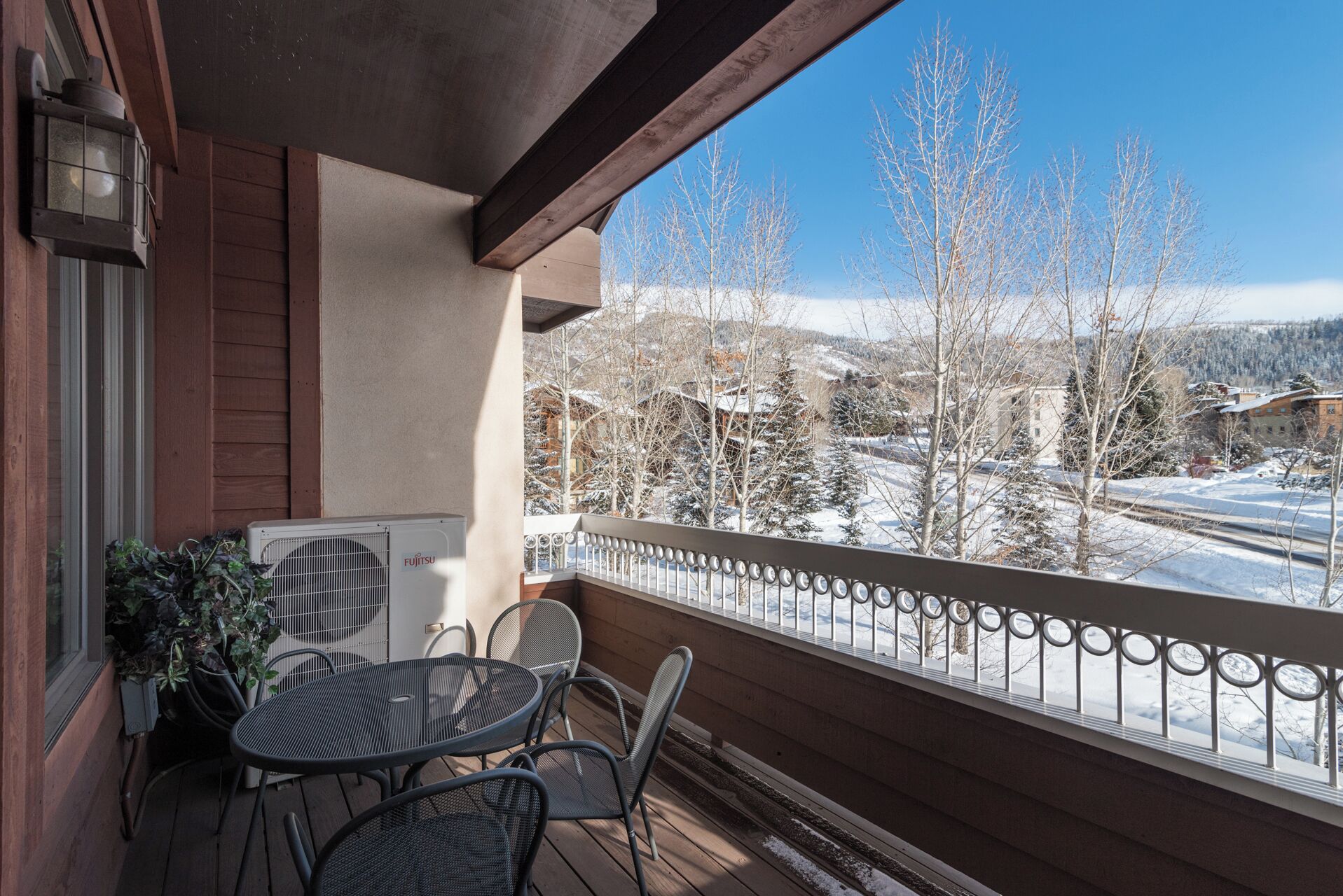 A wooden balcony with a table and chairs, a radiator, and a view of a snowy landscape with trees and buildings.