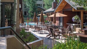 Un patio al aire libre con mesas, sillas, sombrillas y una piscina.