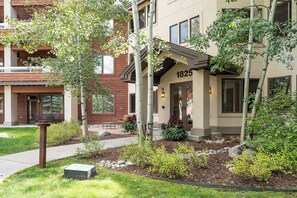 A two-story building with a number '1825' on the front, surrounded by greenery and a small garden area. - CL3306 | Top Floor with Vaulted Ceilings | 10 Hot Tubs | A/C | Pools (Steamboat Springs)