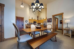 A dining area with a wooden table, chairs, a bench, a chandelier, and a kitchen in the background. - CL3308 | A/C Units | Vaulted Ceilings | Great View | Hot Tubs | Close to Skiing (Steamboat Springs)