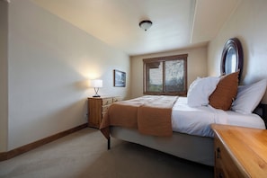 A bedroom with a bed, a nightstand, a lamp, a window with blinds, and a ceiling light. - CL3308 | A/C Units | Vaulted Ceilings | Great View | Hot Tubs | Close to Skiing (Steamboat Springs)