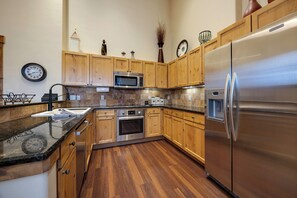 Una cocina con armarios de madera, electrodomésticos de acero inoxidable, microondas, horno, refrigerador y un reloj en la pared.