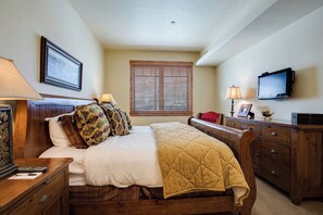 A bedroom with a bed, wooden headboard, bedside tables, a dresser, a television, and a window with blinds. - EL5102 | True Mountain Elegance | Air Chilling | Short Walk to Slopes | Pools (Steamboat Springs)