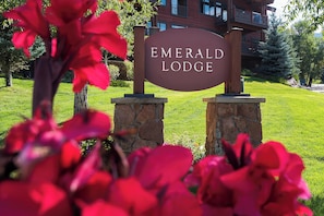 A sign for Emerald Lodge with a stone base and a wooden post, set against a backdrop of a building and greenery. - EL5102 | True Mountain Elegance | Air Chilling | Short Walk to Slopes | Pools (Steamboat Springs)