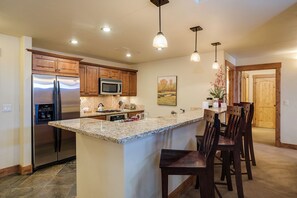 A kitchen with a central island, wooden cabinets, stainless steel appliances, and pendant lighting. - EL5102 | True Mountain Elegance | Air Chilling | Short Walk to Slopes | Pools (Steamboat Springs)