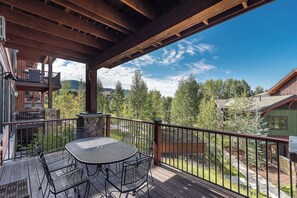 A wooden deck with a table and chairs, overlooking a forested area. - EL5105 | Private Patio with Hot Tub | Air Chilling | Close to Skiing | 4 Pools (Steamboat Springs)