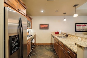 A kitchen with a stainless steel refrigerator, microwave, and stove, wooden cabinets, granite countertop, and a painting on the wall. - EL5110 | Private Hot Tub | 4 Pools | Air Chilling | Close to Skiing (Steamboat Springs)