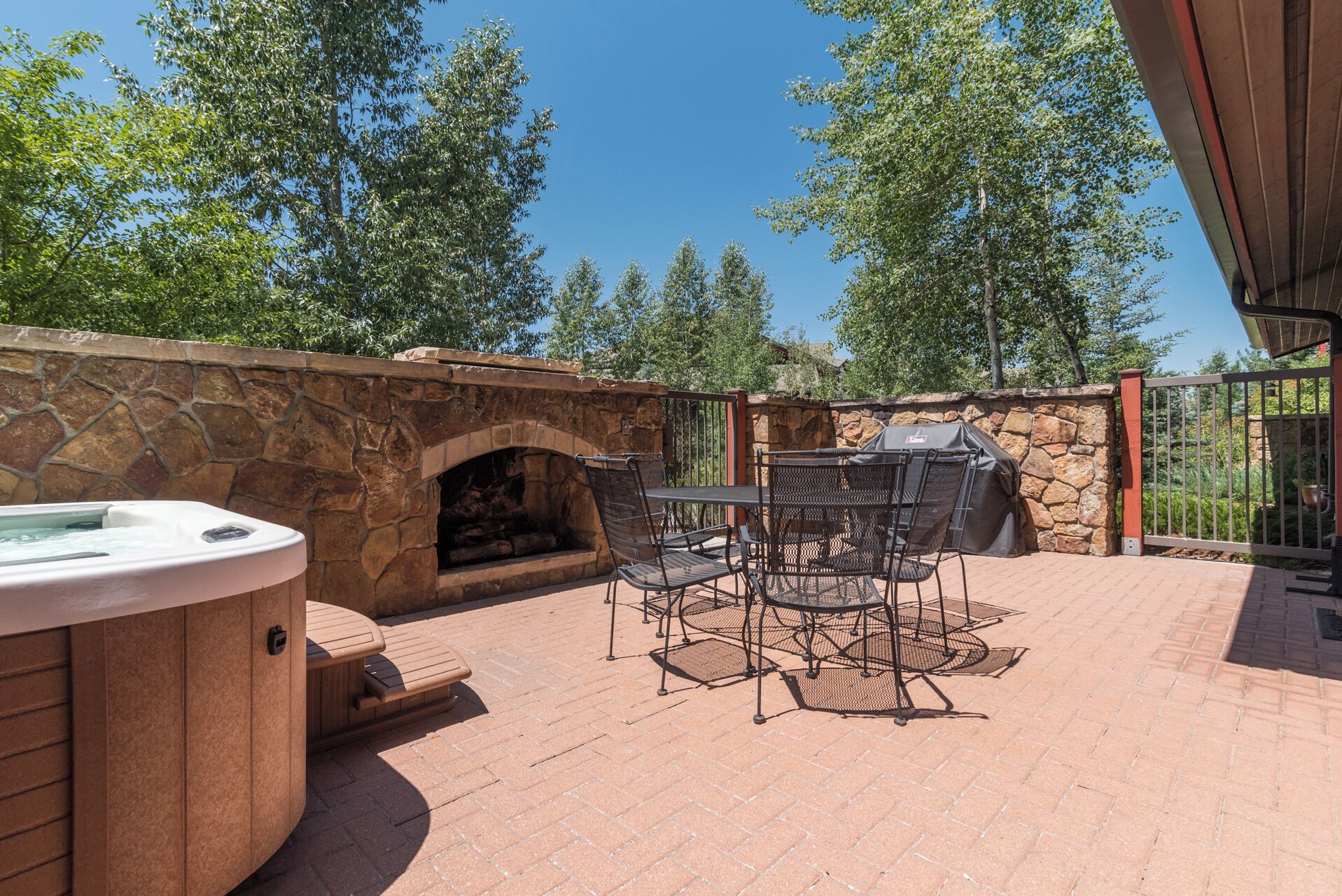 An outdoor patio with a stone fireplace, a hot tub, and a grill area.