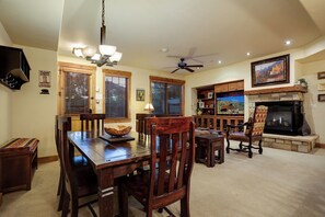 A dining area with a wooden table and chairs, a chandelier, and a fireplace with a stone surround. - EL5112 | Private Patio with Hot Tub | Close to Mtn | Air Chilling | Pools (Steamboat Springs)