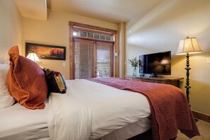 A hotel room with a bed, a television, a lamp, and a window with blinds. - EL5114 | Close to Mtn Activities | Private Hot Tub | Air Chilling | 4 Pools (Steamboat Springs)