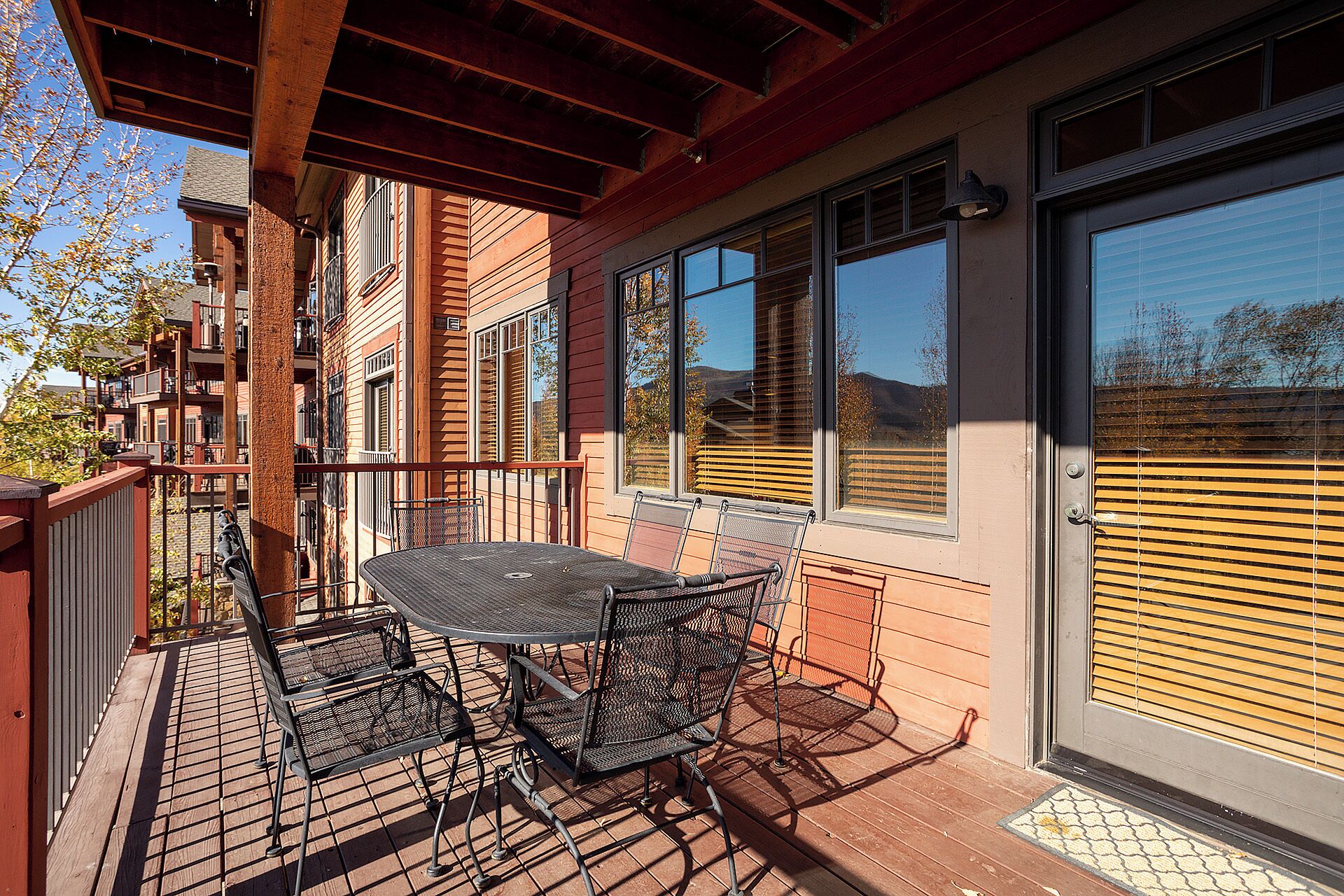 Un patio al aire libre con una mesa y sillas, una pérgola de madera y vistas a una zona residencial.