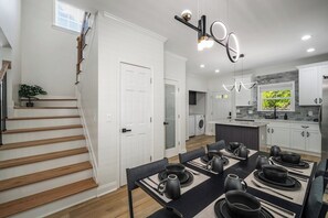 Eine moderne Küche mit weißen Schränken, ein Essbereich mit schwarzem Geschirr und eine Treppe mit Holzstufen.