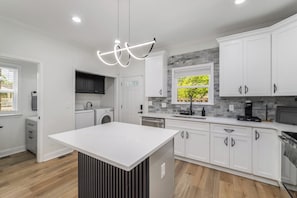 A modern kitchen with white cabinetry, a central island, and a stone backsplash. - The Buford Luxe | Game Room + Office | 3BR (Atlanta)