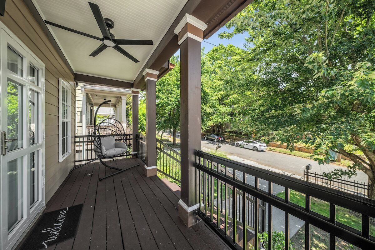 A covered porch with a ceiling fan, a rocking chair, and a view of a street with cars and trees.