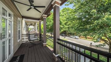 A covered porch with a ceiling fan, a rocking chair, and a view of a street with cars and trees.