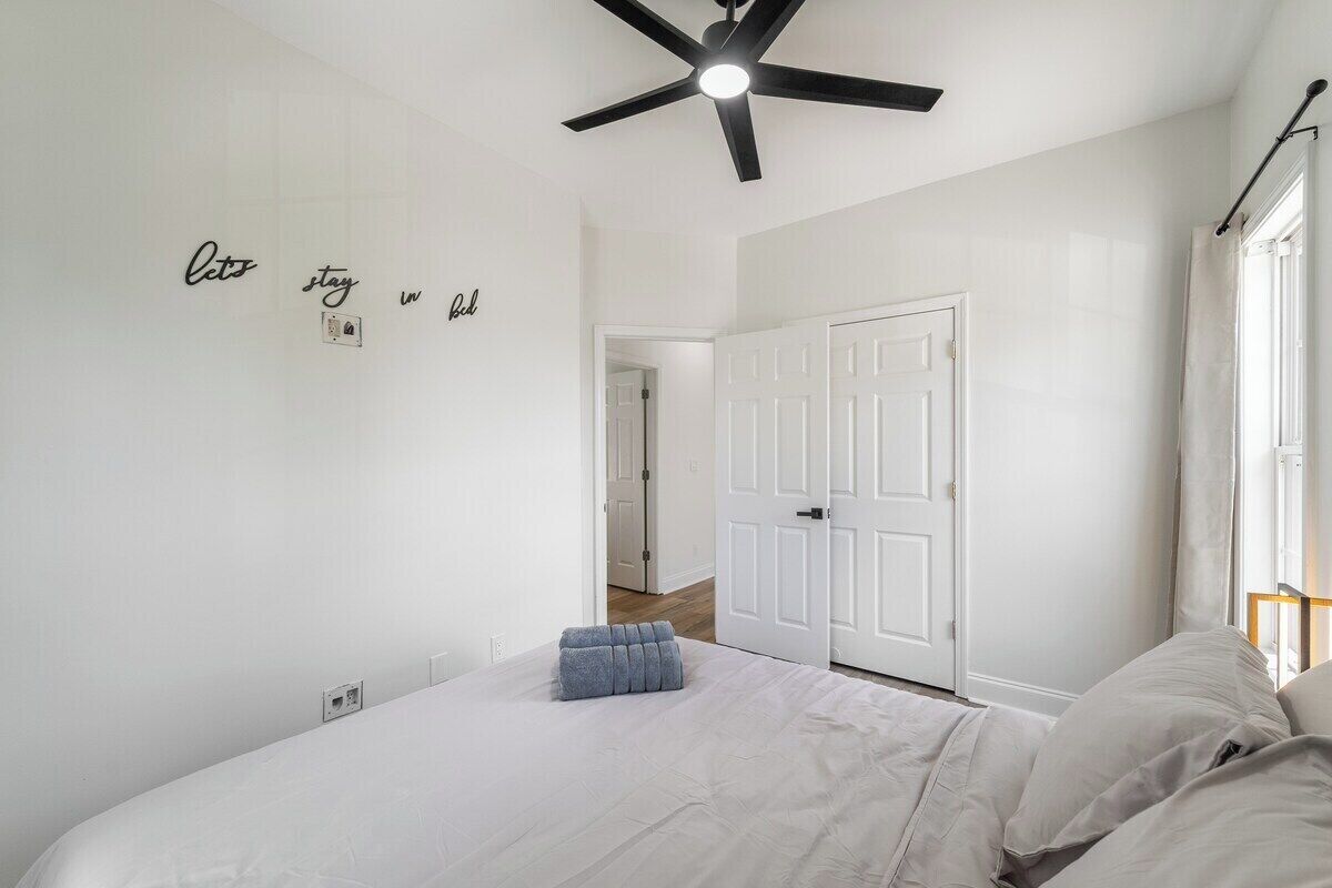 Un dormitorio con cama, ventilador de techo, una puerta blanca y una pared con texto.
