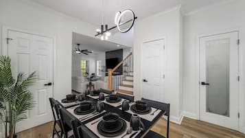 Un comedor con una paleta de colores blanco y negro, una escalera al fondo y una planta en maceta a la izquierda.