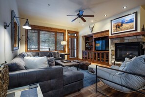 A living room with a fireplace, a ceiling fan, and a large window with blinds. - EL5208 | Spacious with Mountain View | Air Chilling | Close to Mtn | Hot Tubs (Steamboat Springs)
