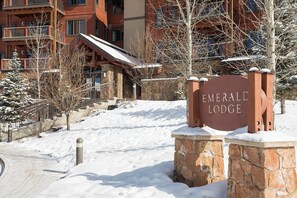 Ein verschneiter Eingang zum Emerald Lodge mit einer Steinmauer und einem Metallgitter.