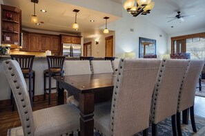 A dining area with a wooden table and upholstered chairs, a kitchen with wooden cabinets, and a ceiling fan. - EL5303 | Mtn Getaway | Resort Amenities | 2 King Suites | Air Chilling (Steamboat Springs)