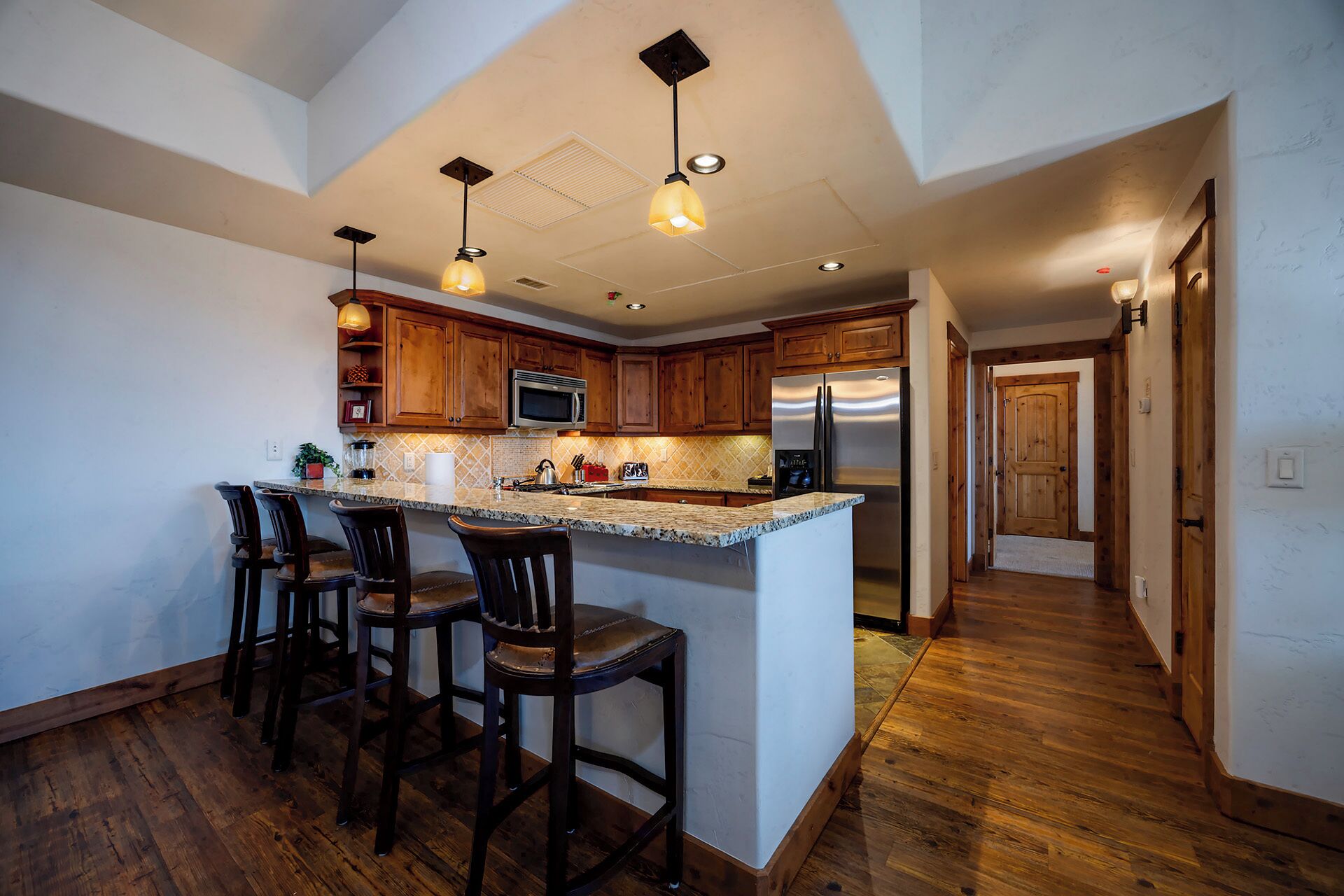 A kitchen with a central island, wooden bar stools, a microwave, and a refrigerator.