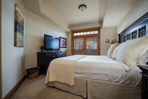 Ein Schlafzimmer mit einem Bett, einem Fernseher auf einer Kommode, einem Fenster mit Jalousien und einer Deckenleuchte.