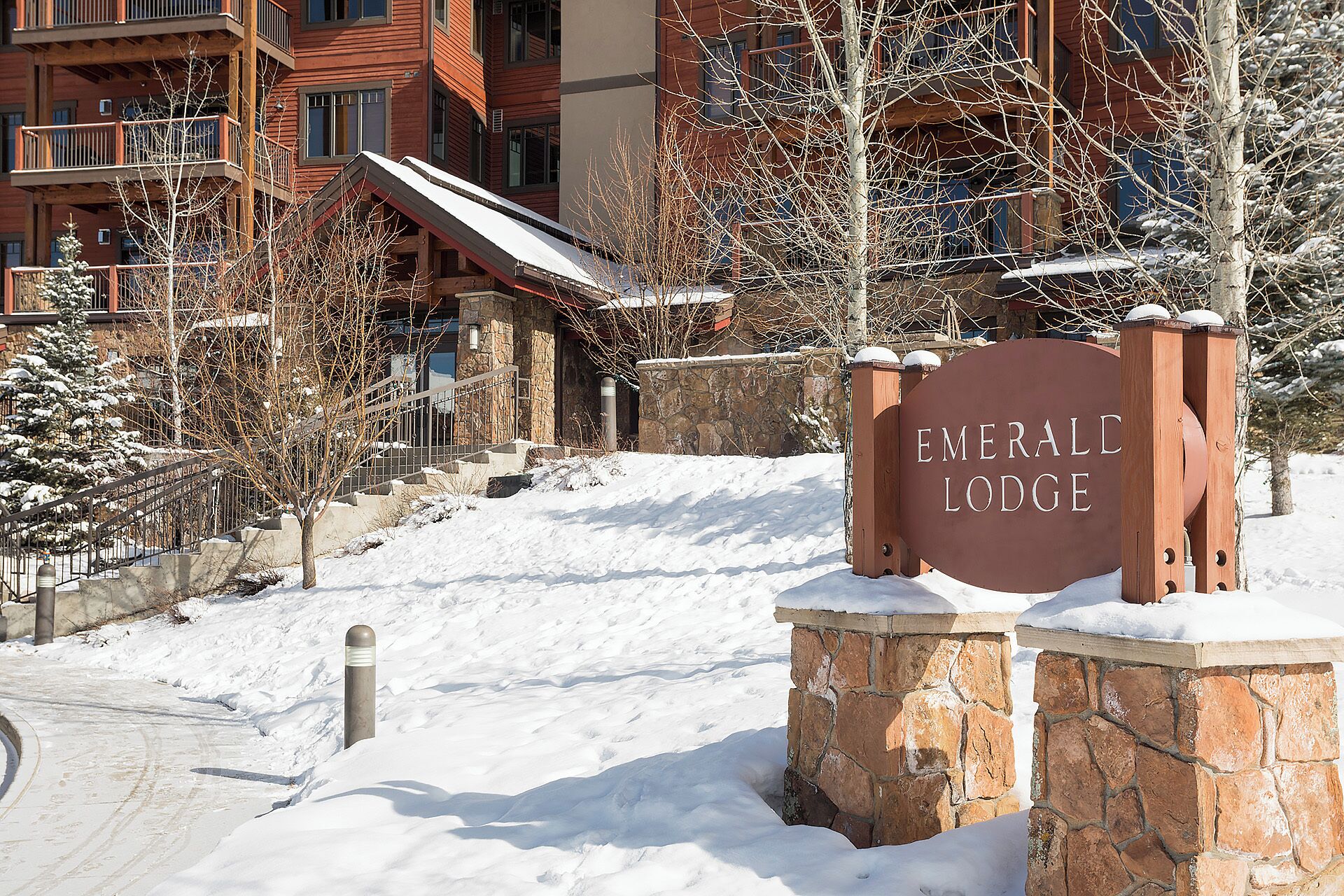 Een besneeuwde ingang van Emerald Lodge, met een stenen muur en een metalen hek.