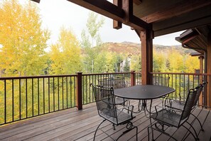 A wooden deck with metal chairs and a table, overlooking a forested area with autumn foliage. - EL5305 | Top Floor with Mountain Views | Air Chilling | 10 Hot Tubs | 4 Pools (Steamboat Springs)